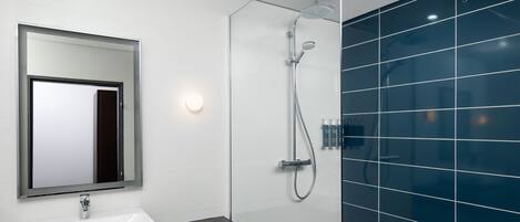 A modern bathroom with a white sink, a large mirror, a glass-enclosed shower, and blue-tiled walls.