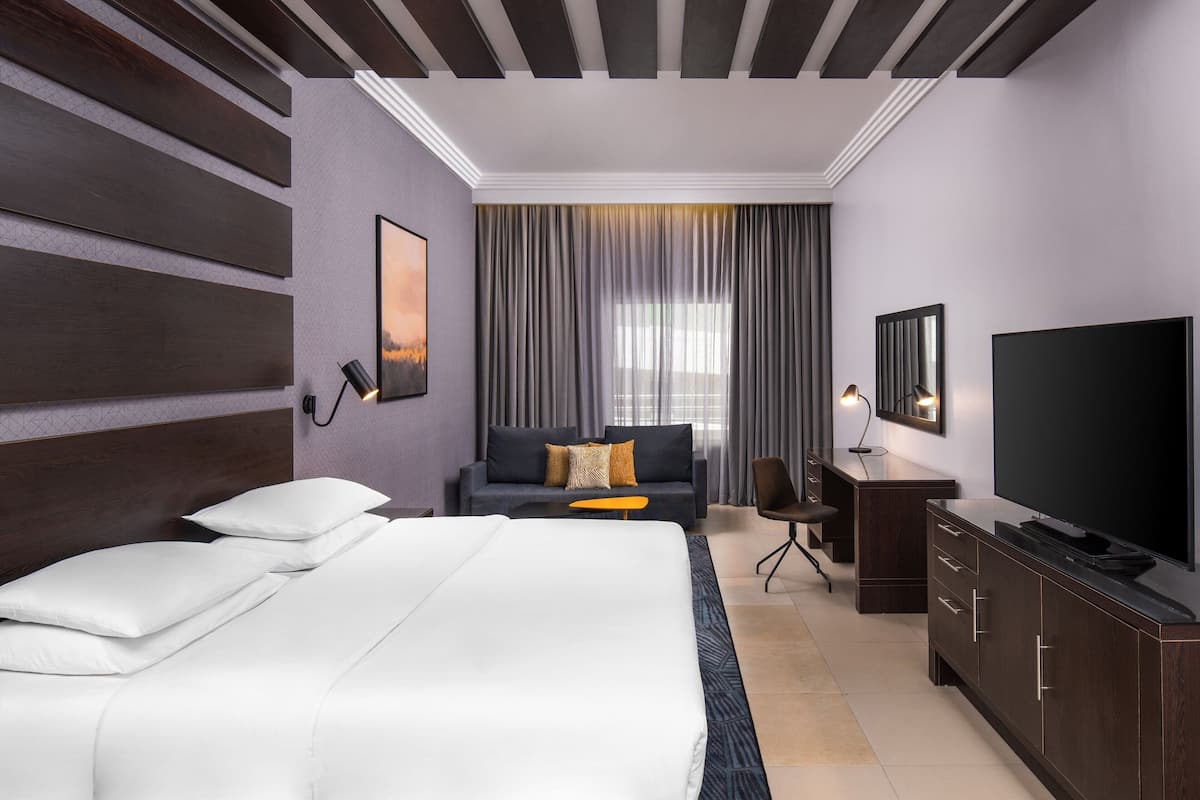 A hotel room with a large bed, a sofa, a TV, and a desk.