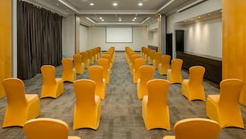 Une salle de conférence avec des rangées de chaises jaunes, un grand écran et un sol recouvert de moquette.