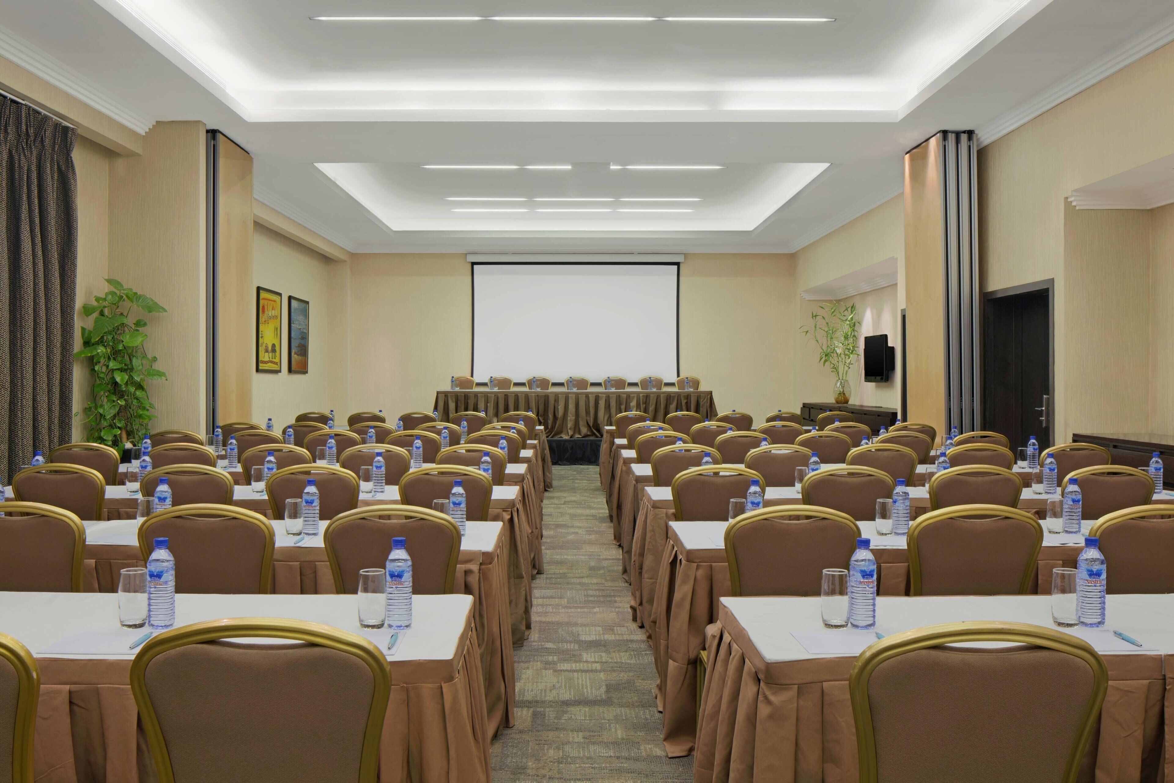 A conference room with rows of tables and chairs, each with a water bottle.