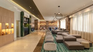 A hotel lobby with a long row of sofas, a reception desk, and a seating area with a green carpet. - Four Points by Sheraton Lagos (Lagos)