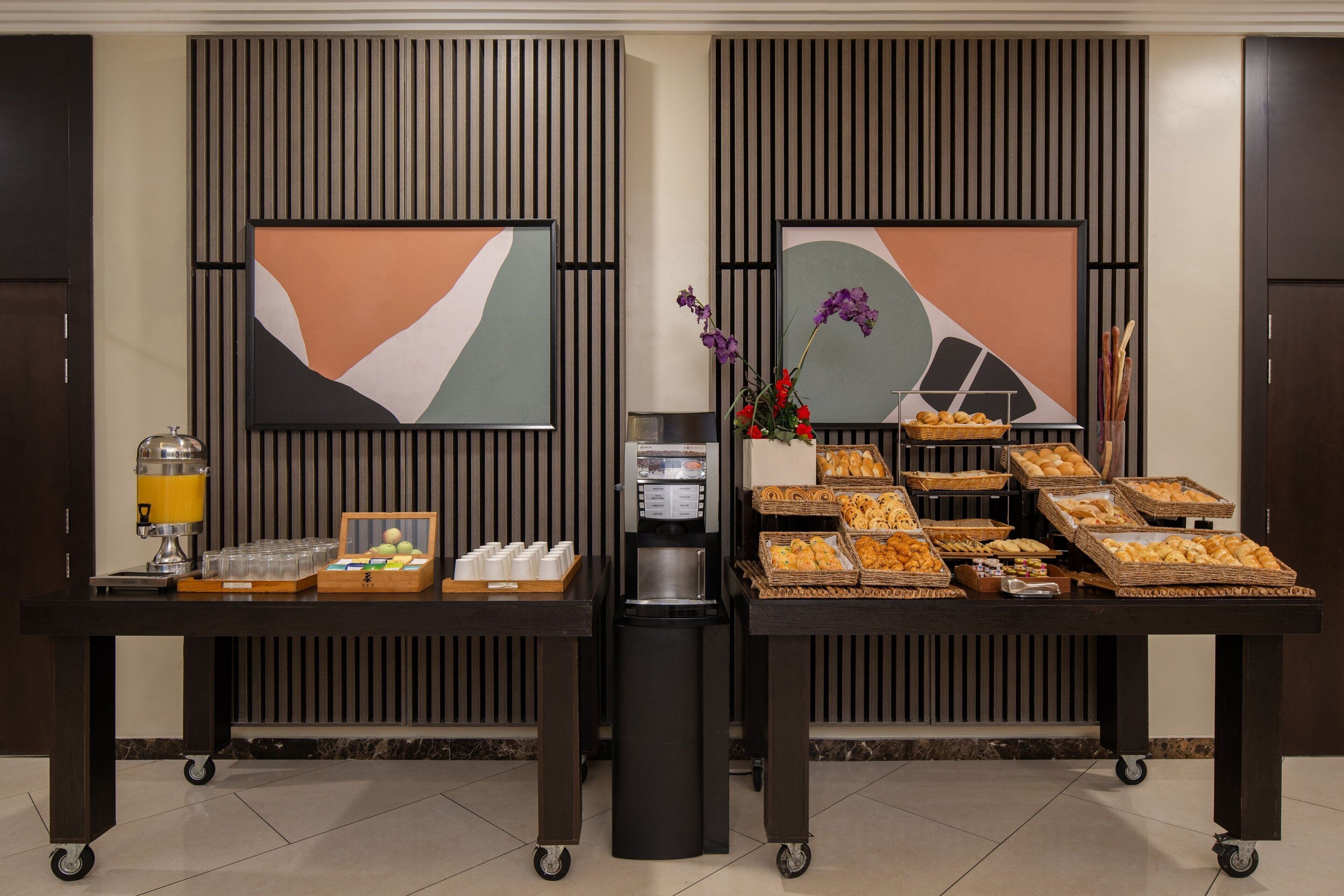 A buffet setup with various food items and a coffee machine, set against a backdrop of abstract art and vertical paneling.