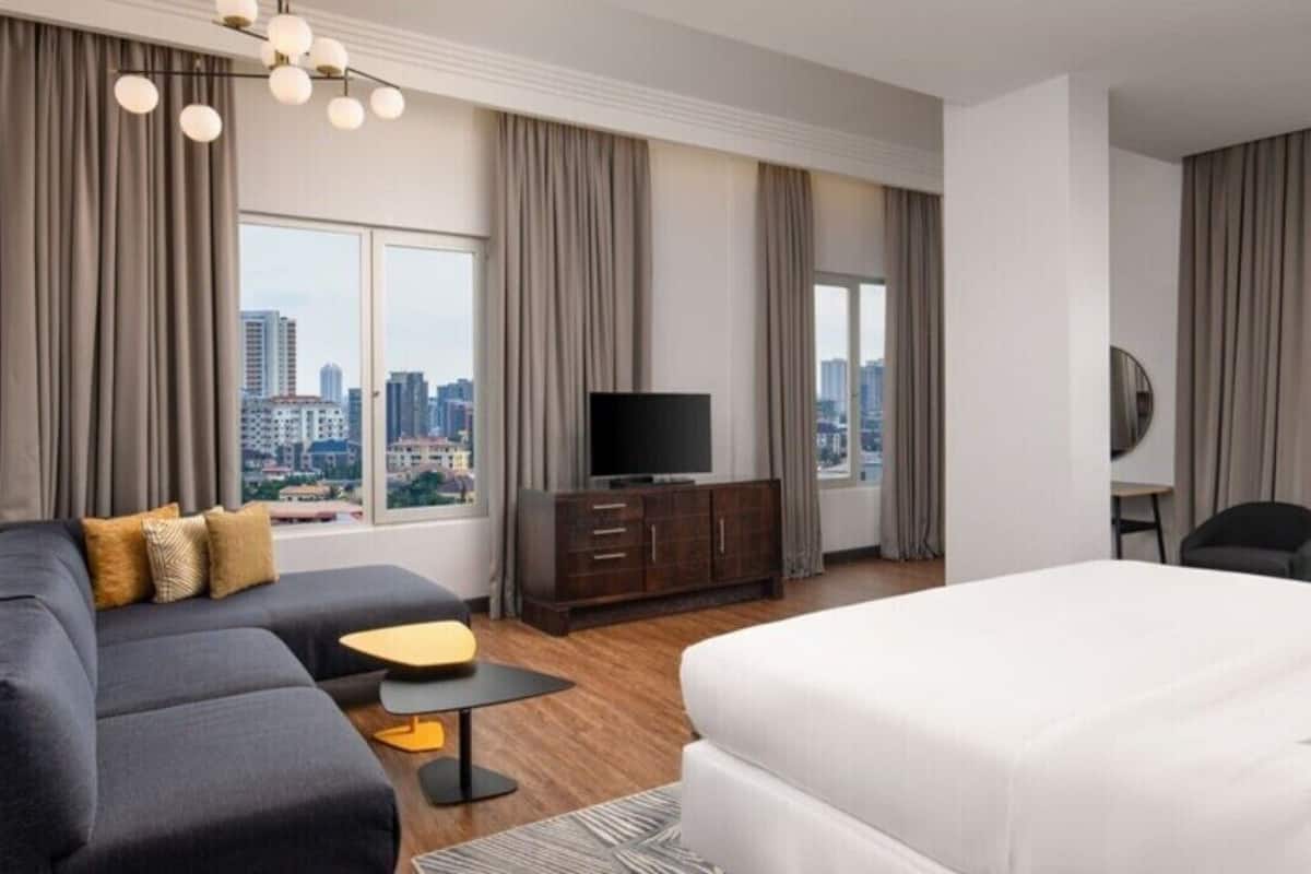 A modern hotel room with a large bed, a sofa, a TV, and a view of the city.