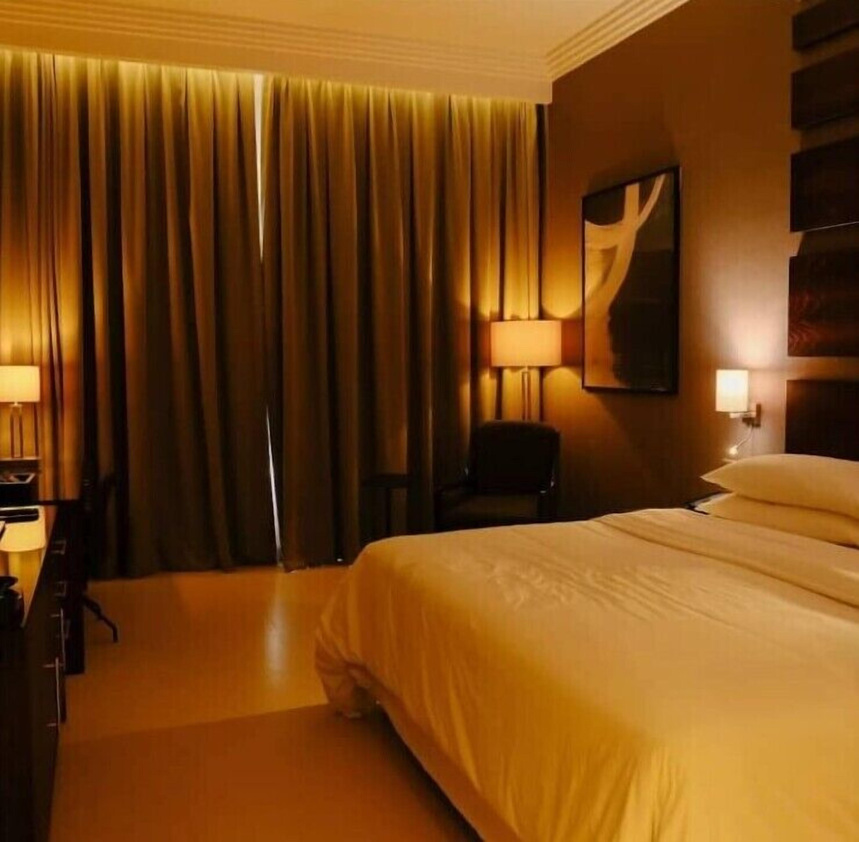 A hotel room with a large bed, a desk, a chair, and a lamp.