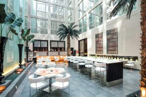 Un espacio interior amplio con techos altos, ventanas grandes y una zona de estar central con mesas y sillas.