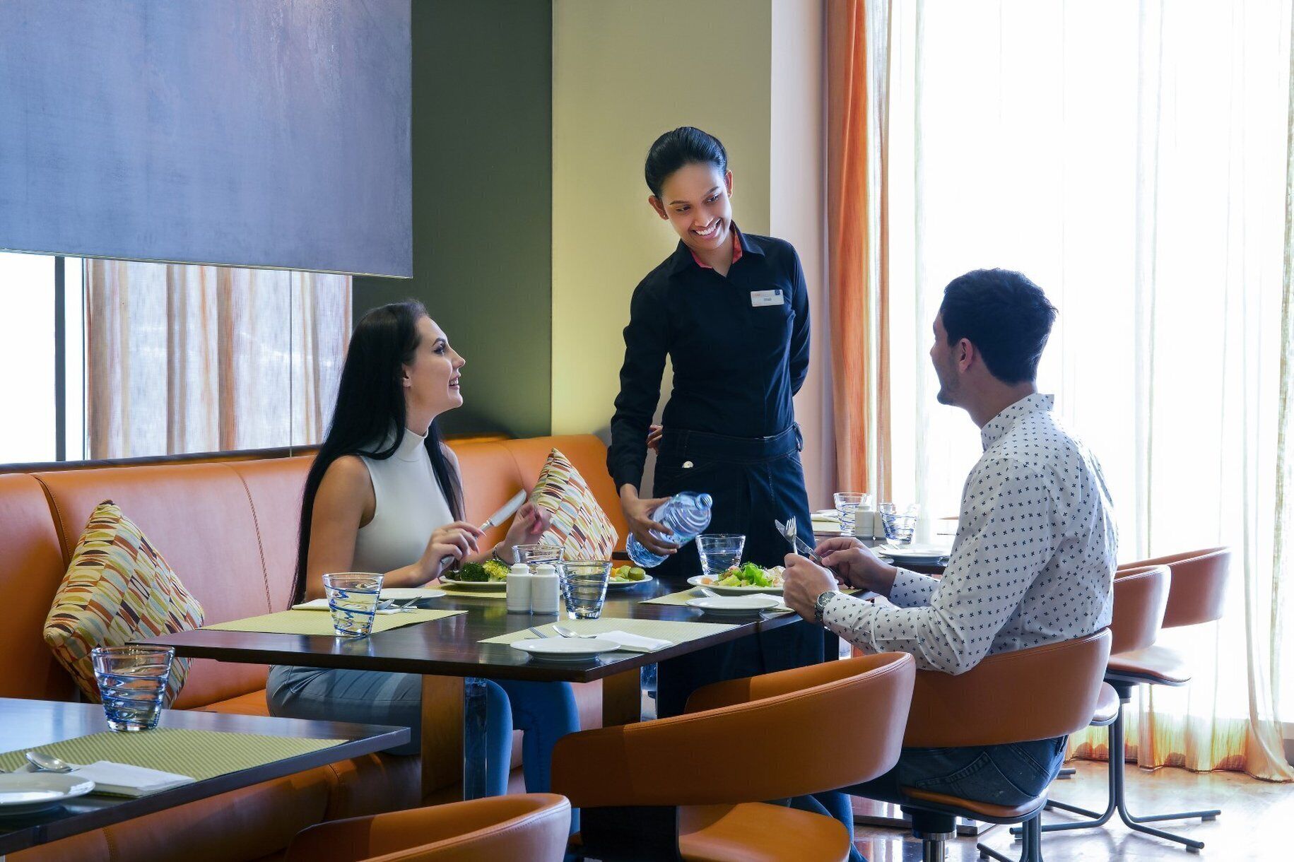 Une scène de restaurant avec une table dressée pour deux personnes, un serveur et un client.