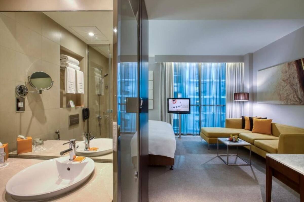 A hotel room with a bathroom, a bed, a TV, and a seating area.