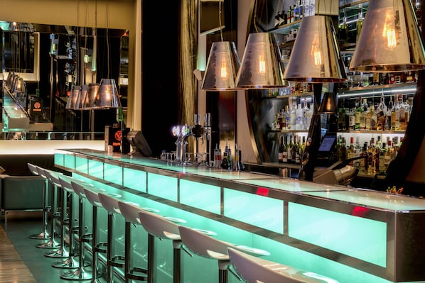 Uma área de bar com vários bancos, balcão e iluminação suspensa.