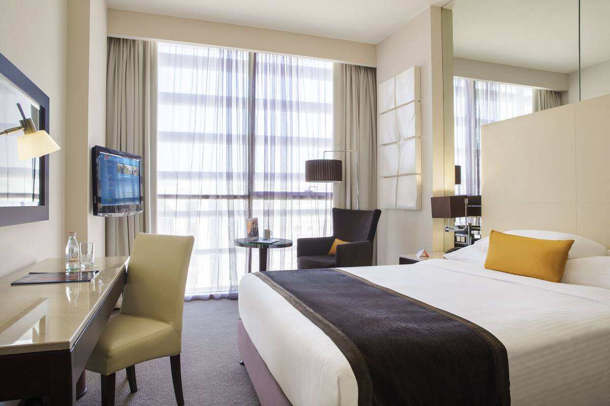 A hotel room with a large bed, a desk with a chair, a TV, and a window with curtains.