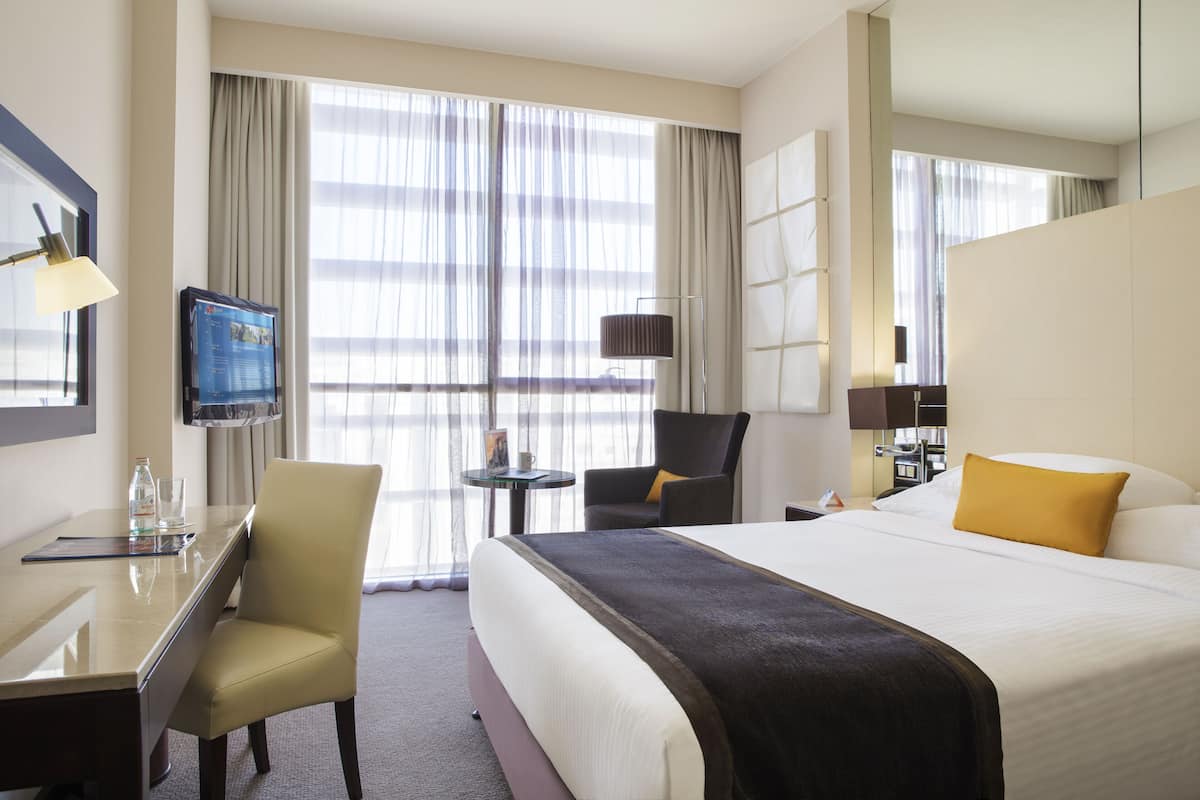 A hotel room with a large bed, a desk with a chair, a TV, and a window with curtains.