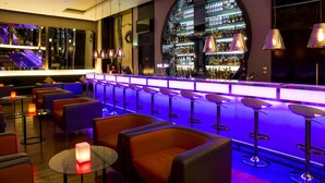 A bar area with multiple stools, a bar counter, and a variety of bottles. - Centro Barsha (Dubai)