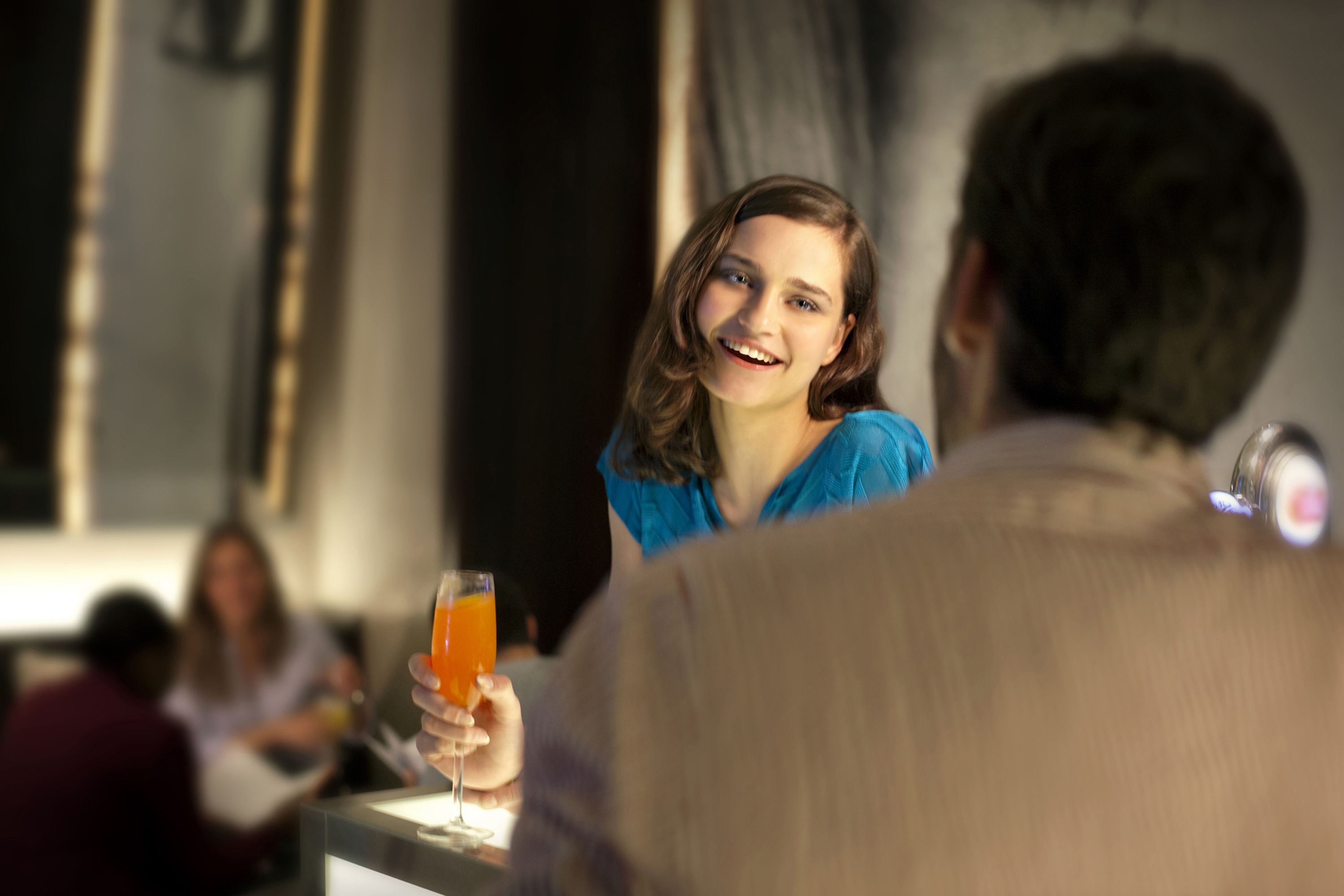 A person holding a glass of orange juice at a bar in a hotel.
