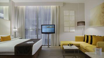 Quarto de hotel com cama, televisão, sofá, mesa de centro e abajur.