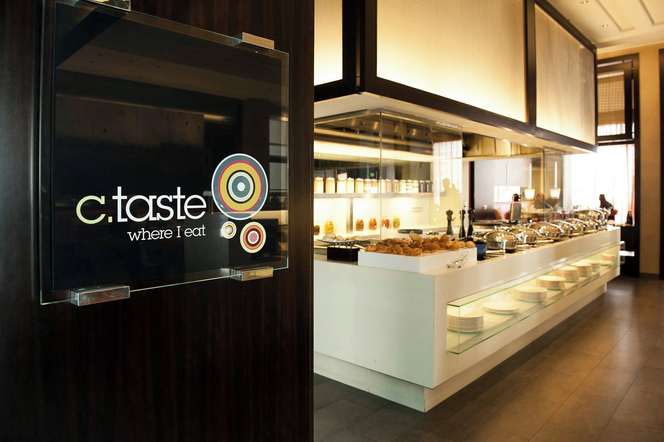 Zona de bufé con un expositor de vidrio y un letrero que dice 'c.taste where I eat'.