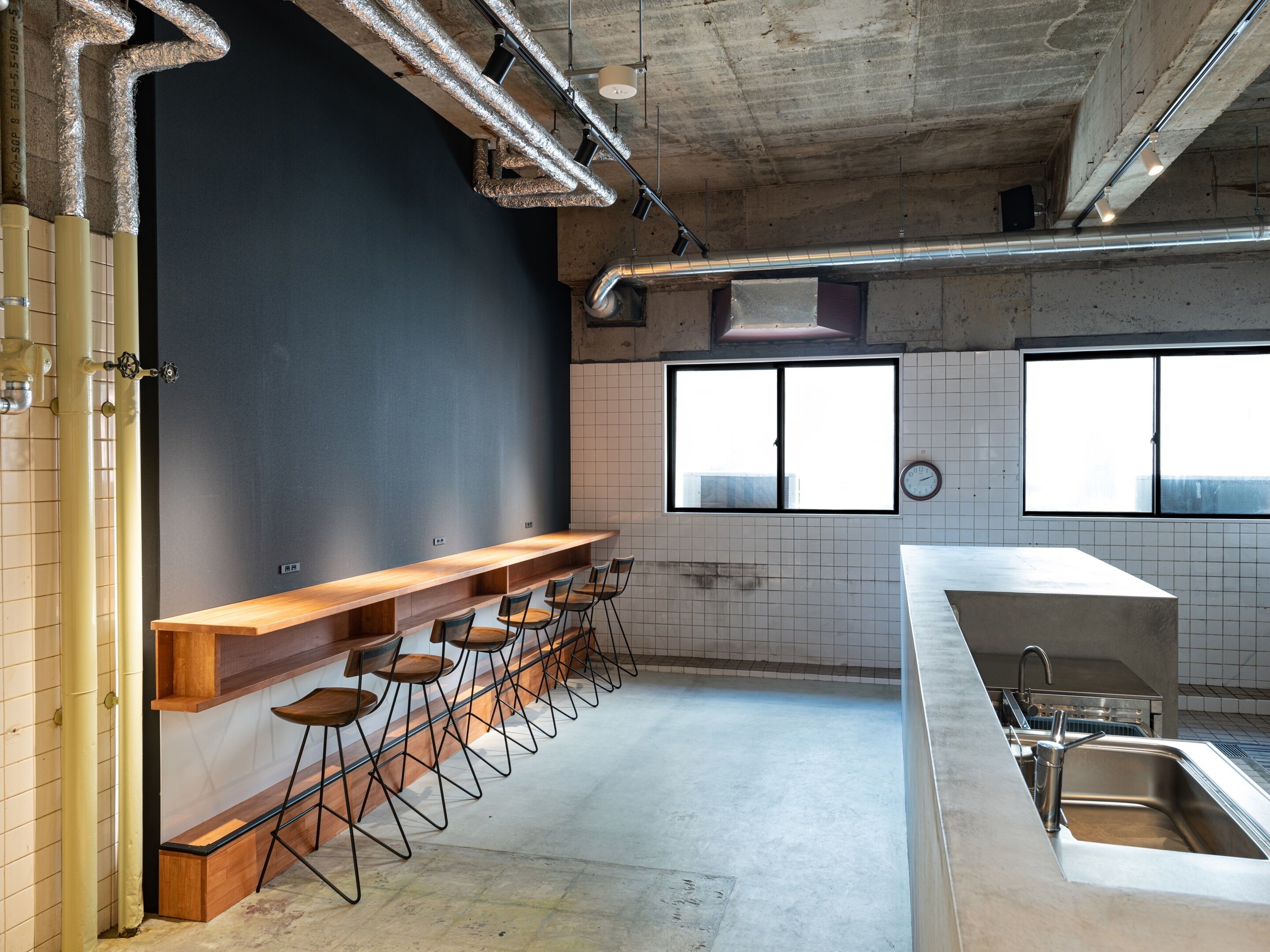 A modern kitchen with a bar area, large windows, and exposed ductwork.