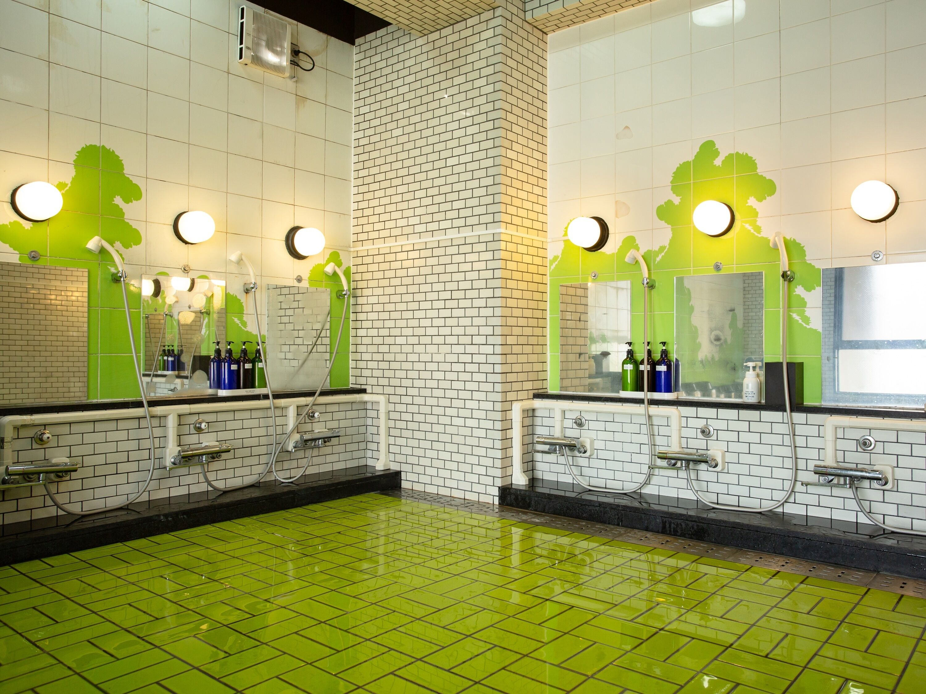 A bathroom with green-tiled floors, white and green-tiled walls, and two sinks with mirrors.