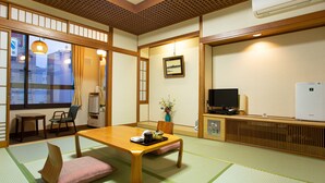 Een traditionele Japanse kamer met tatami vloeren, een lage houten tafel, een televisie en een witte koelkast.