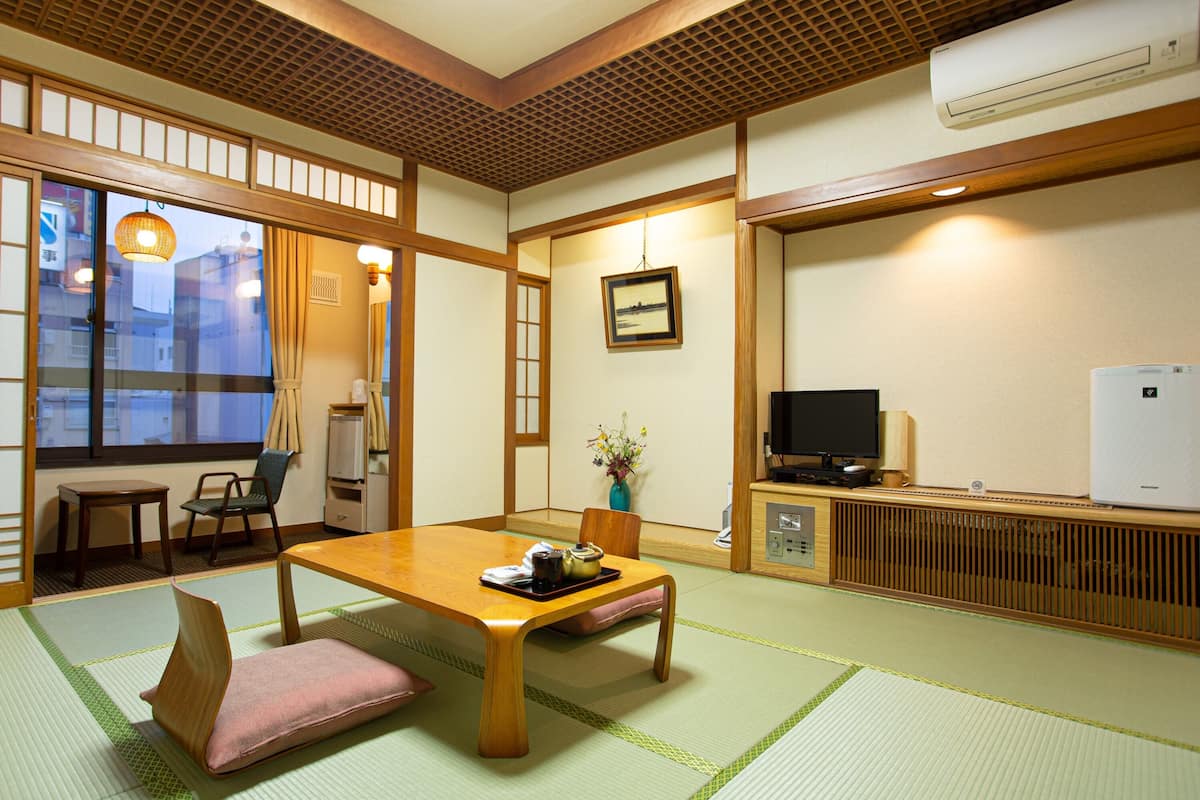 A traditional Japanese room with tatami flooring, a low wooden table, a television, and a white refrigerator.