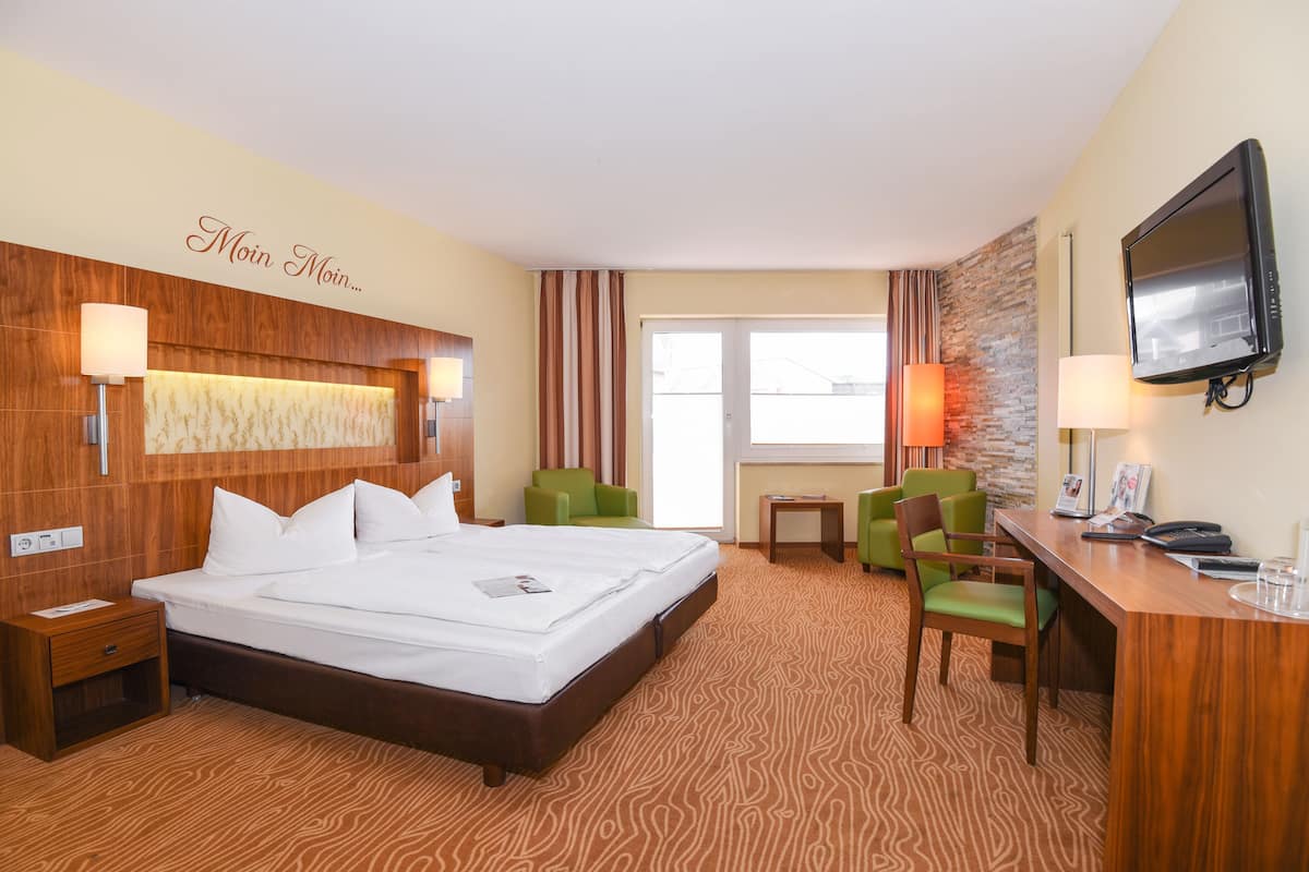 A hotel room with a large bed, a desk with a chair, a television, and a window with curtains.