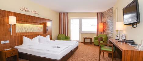 A hotel room with a large bed, a desk with a chair, a television, and a window with curtains.