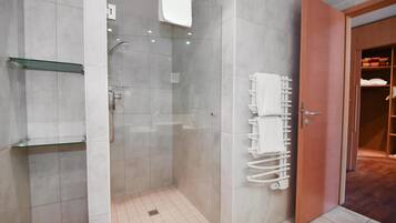 Un baño moderno con ducha envuelta en vidrio, repisa de vidrio, perchero y puerta de madera que da a un armario.