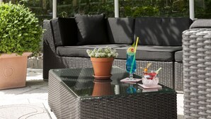 Un área de estar al aire libre con una mesa de vidrio, dos plantas en macetas y una bebida sobre la mesa.