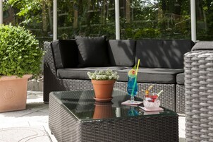 Ein Sitzbereich im Freien mit einem Tisch mit Glasplatte, zwei Blumentöpfen und einem Getränk darauf.