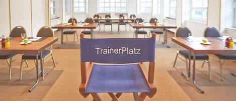 A conference room with tables, chairs, and a blue chair labeled "TrainerPlatz".