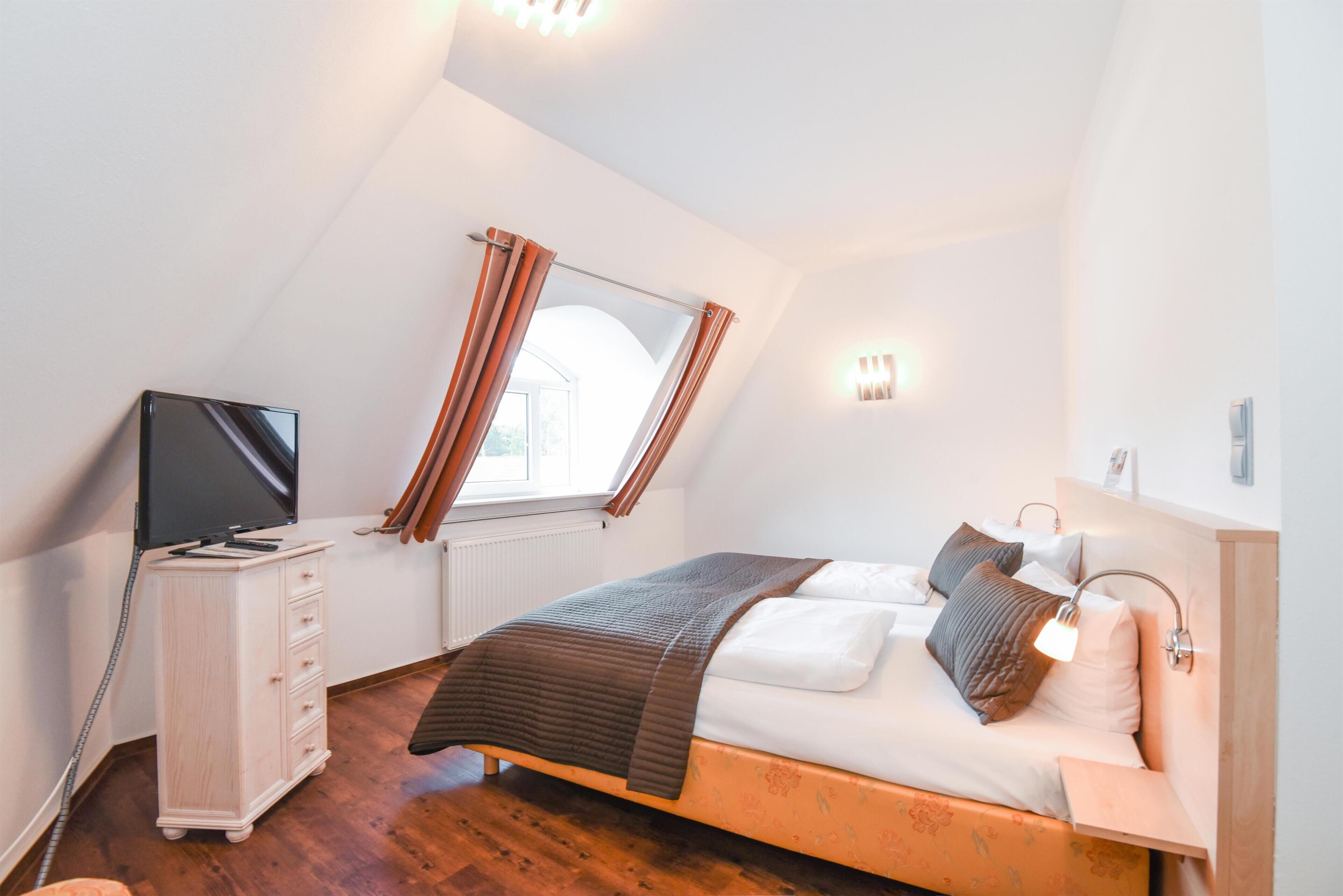 Un dormitorio con cama, televisor, cómoda y ventana con cortinas.
