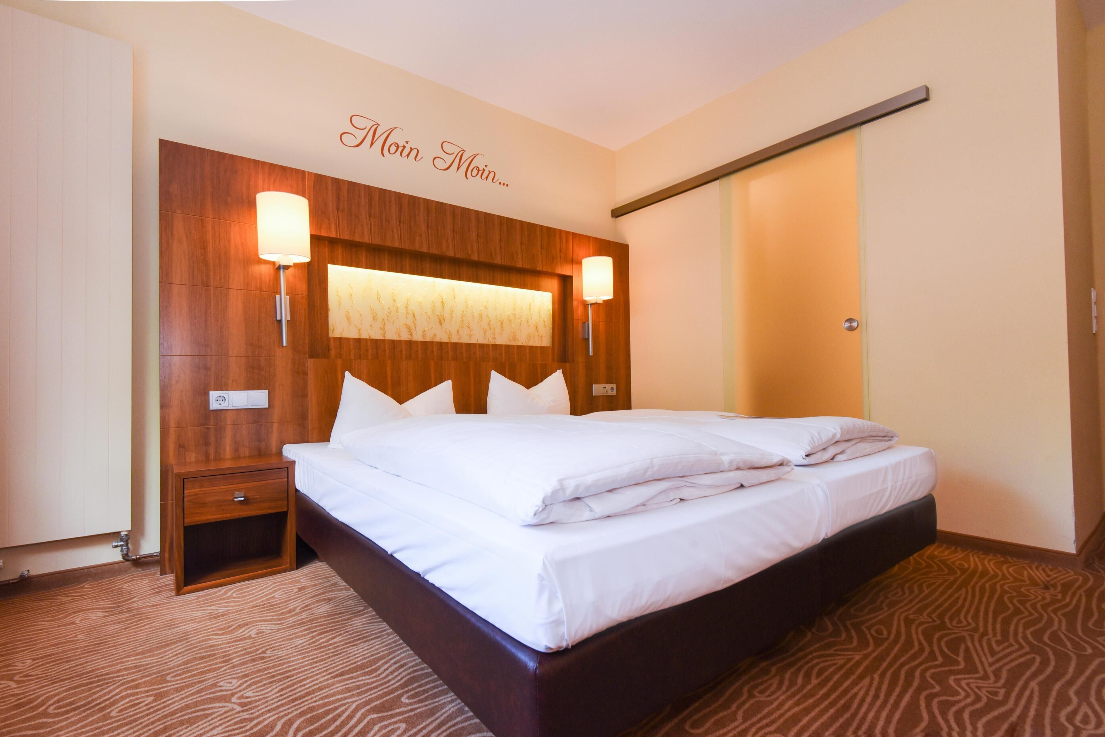 A hotel room with a large bed, wooden headboard, bedside lamps, and a wall-mounted light fixture.