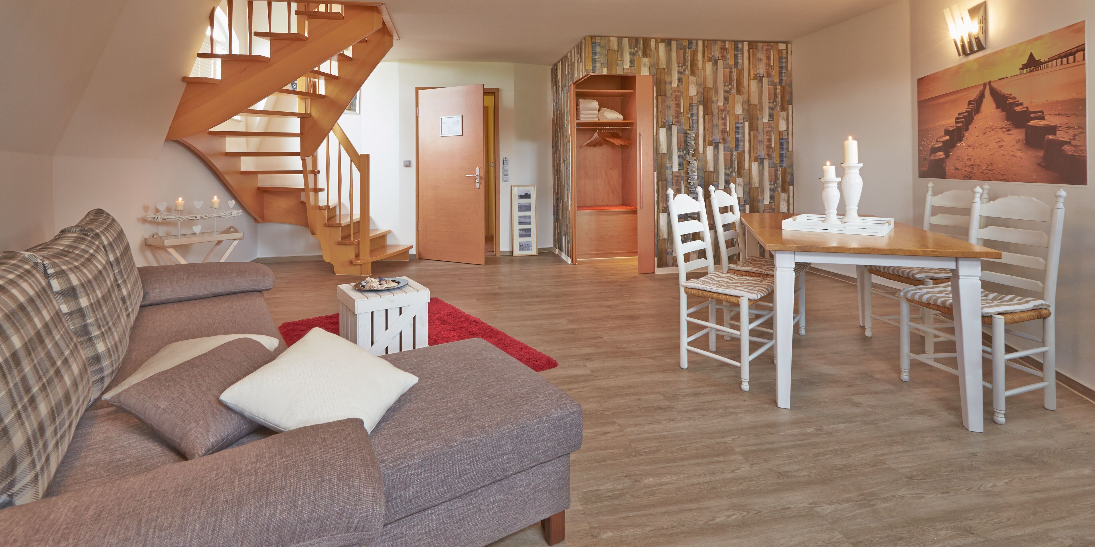 Un salon avec un escalier, un coin repas avec des chaises blanches et une table en bois.
