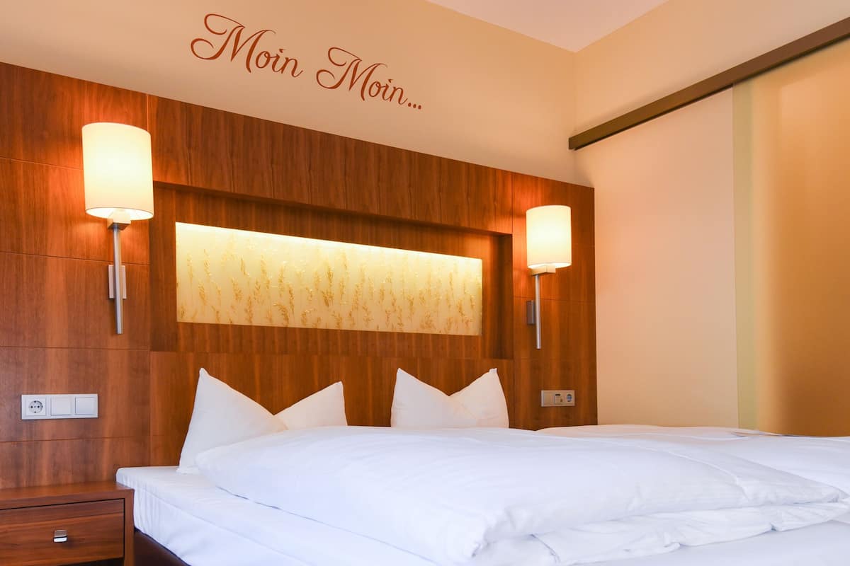 A hotel room with a large bed, wooden headboard, two bedside lamps, and a patterned carpet.
