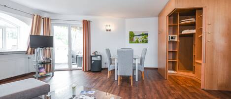 Una sala de estar moderna con una mesa de centro de vidrio, un sofá gris, una zona de comedor con una mesa y sillas, un armario de madera y un televisor sobre un mueble.