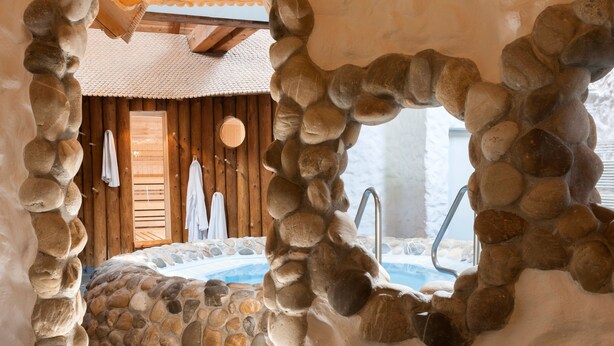 Un baño con paredes de piedra, una bañera y una puerta de madera.