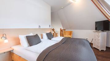 Een slaapkamer met een bed, nachtkastje, lamp, stoel, televisie en een dressoir.