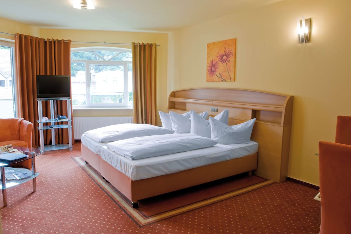 A hotel room with a bed, a TV on a stand, a chair, and a window with curtains.