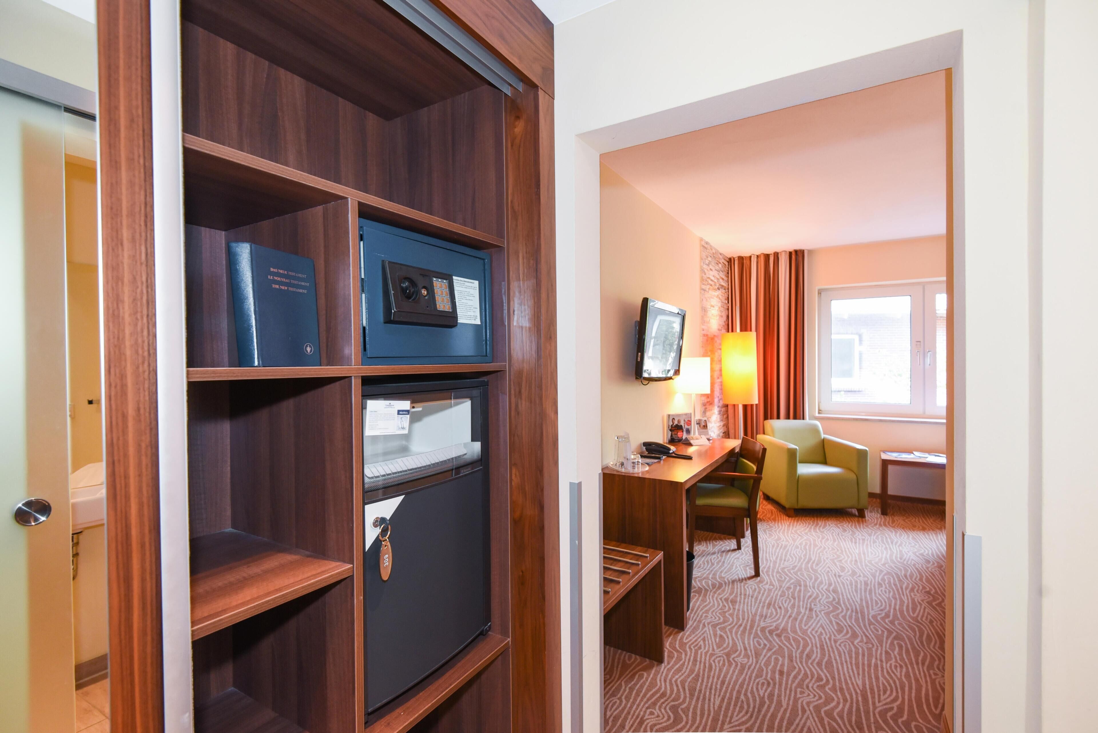 Habitación de hotel con un armario de madera, un escritorio con lámpara, un televisor y un sillón verde.