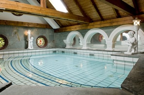 An indoor swimming pool with tiled flooring, wooden beams, and decorative statues.