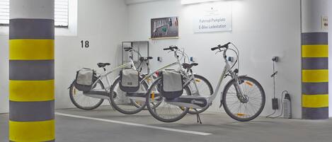 Un'area di parcheggio con biciclette, un cartello che segnala una stazione di biciclette elettriche e un espositore a parete per attrezzi.