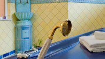 Ein Badezimmer mit blauer Ablagefläche, einer goldfarbenen Duschbrause und einer Wand mit Uhr und Pflanzen.