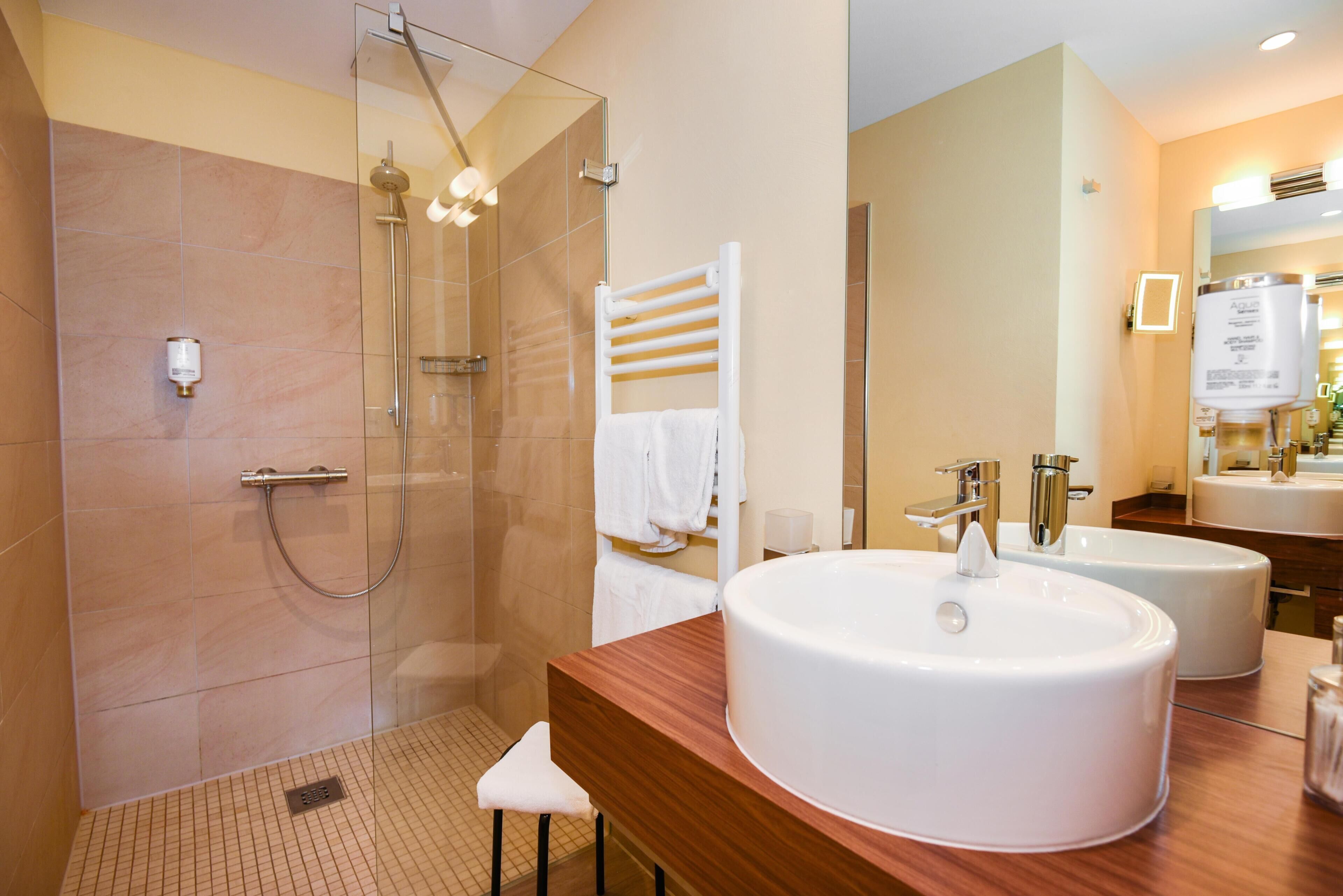 A modern bathroom with a glass-enclosed shower, a wooden vanity with two sinks, and a white towel rack.
