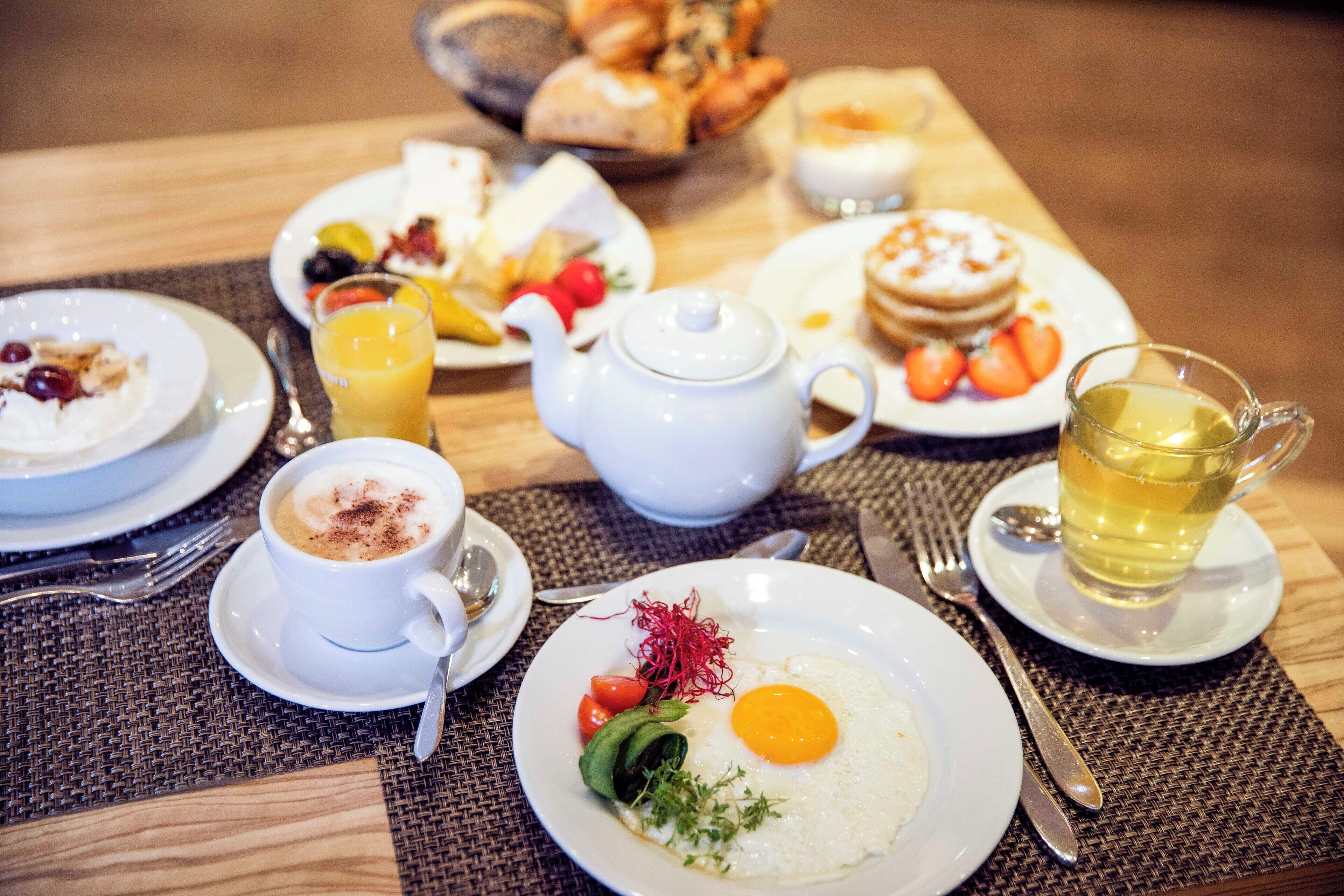 A breakfast setting with plates of food, a teapot, and a cup of tea.