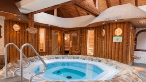Una cabaña de madera con hidromasaje de baldosas de piedra, paredes de madera y un interior rústico.