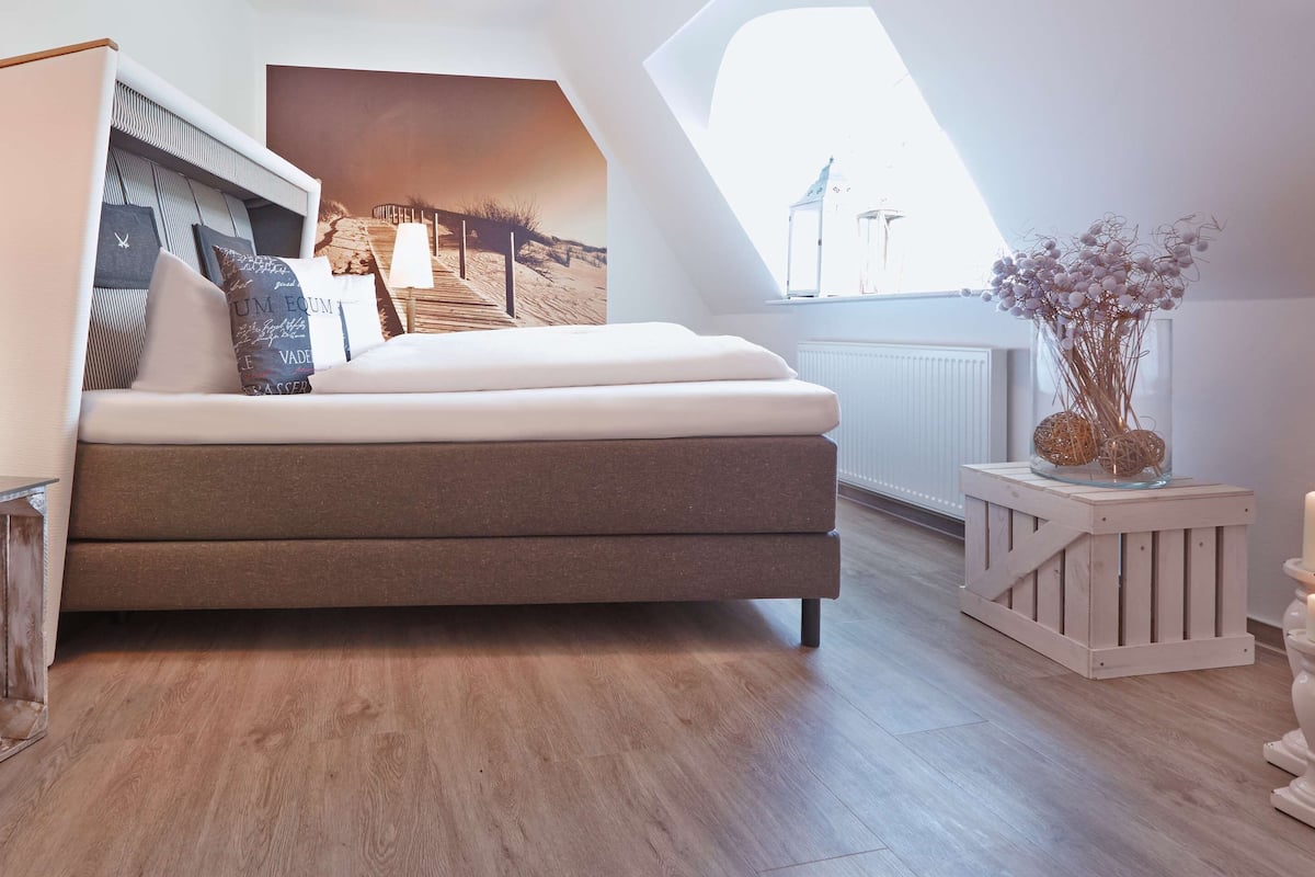 A bedroom with a bed, bedside tables, a nightstand, a window with a view, and a wall-mounted artwork.