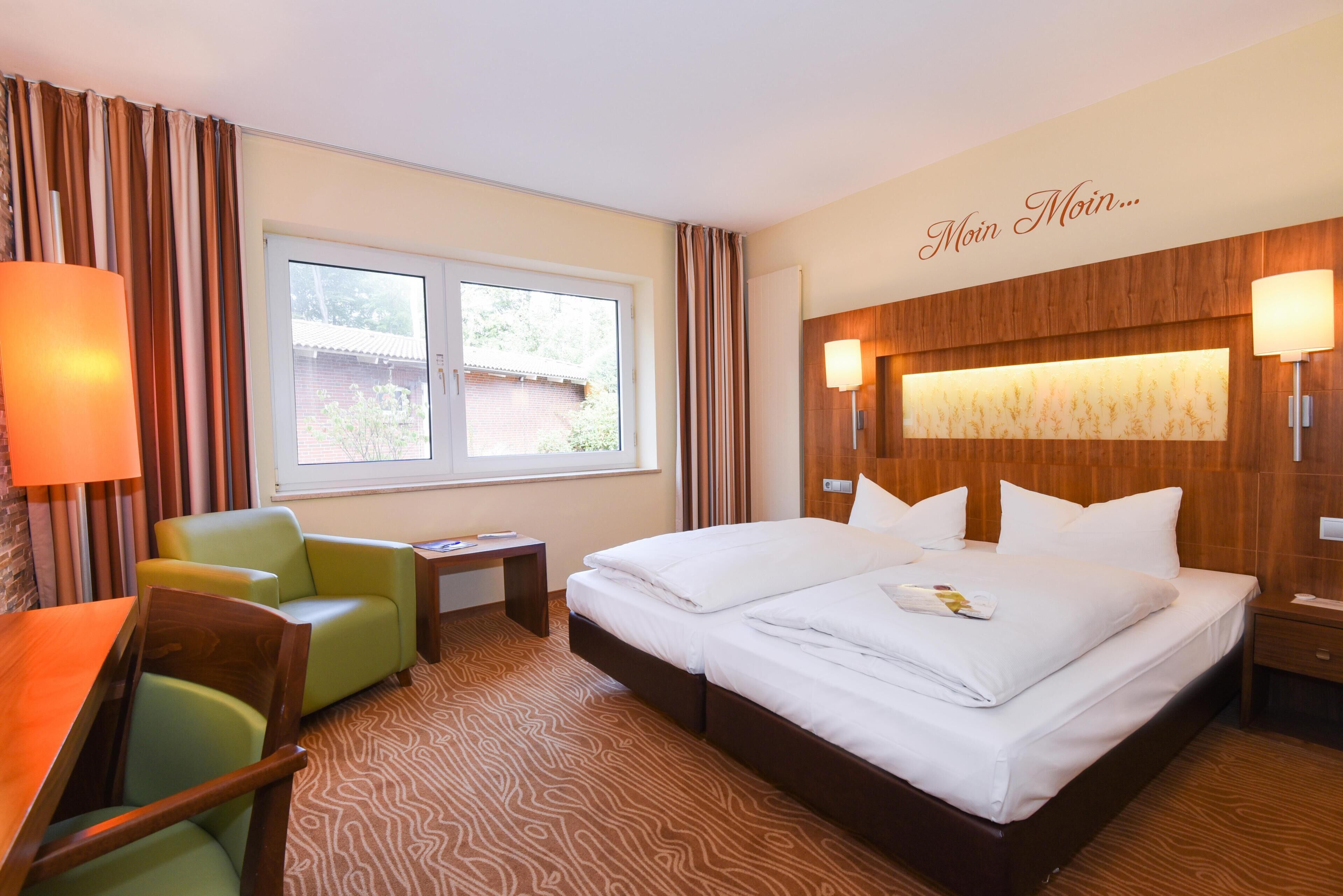 A hotel room with a bed, a desk, a chair, a window, and a wall-mounted lamp.