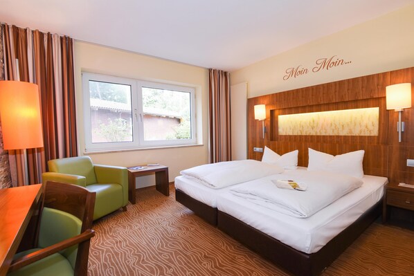 Habitación de hotel con cama, escritorio, silla, ventana y lámpara de pared.