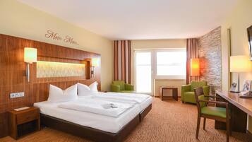 A hotel room with a large bed, two green chairs, a desk, and a stone accent wall.