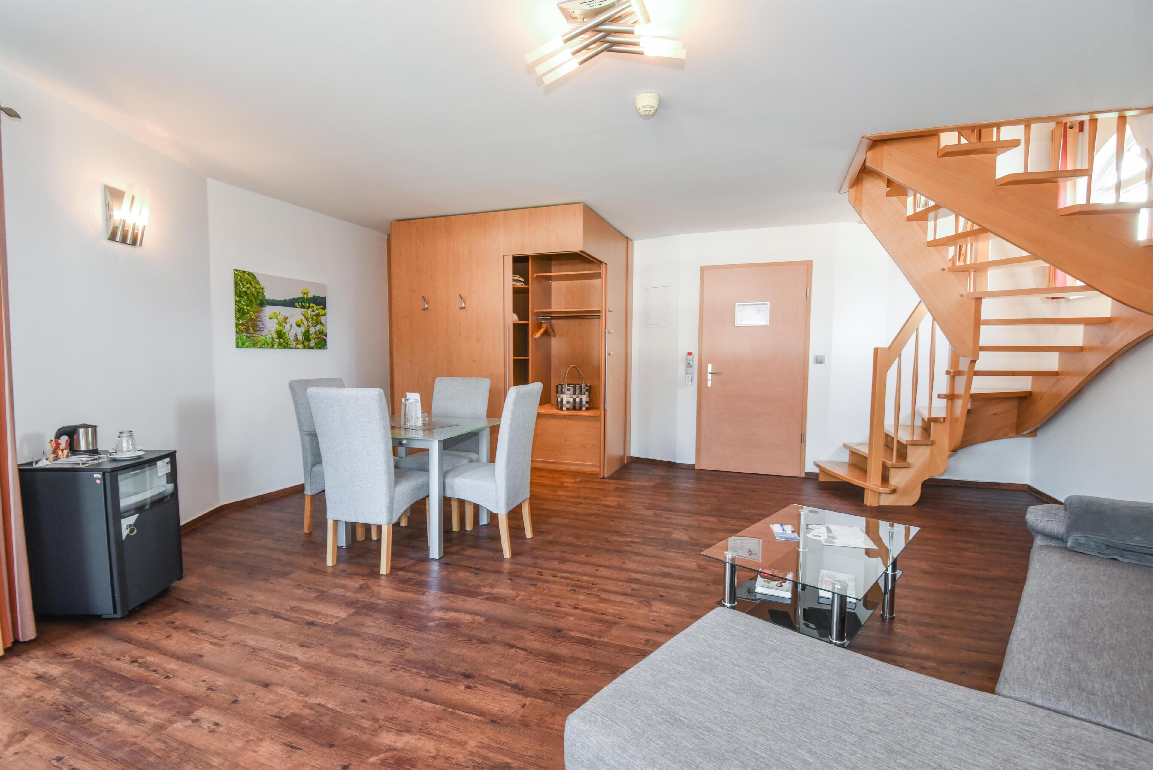 A modern living room with a wooden staircase, a dining area with a glass table, and a cozy seating area.