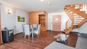 A modern living room with a wooden staircase, a dining area with a glass table, and a cozy seating area.