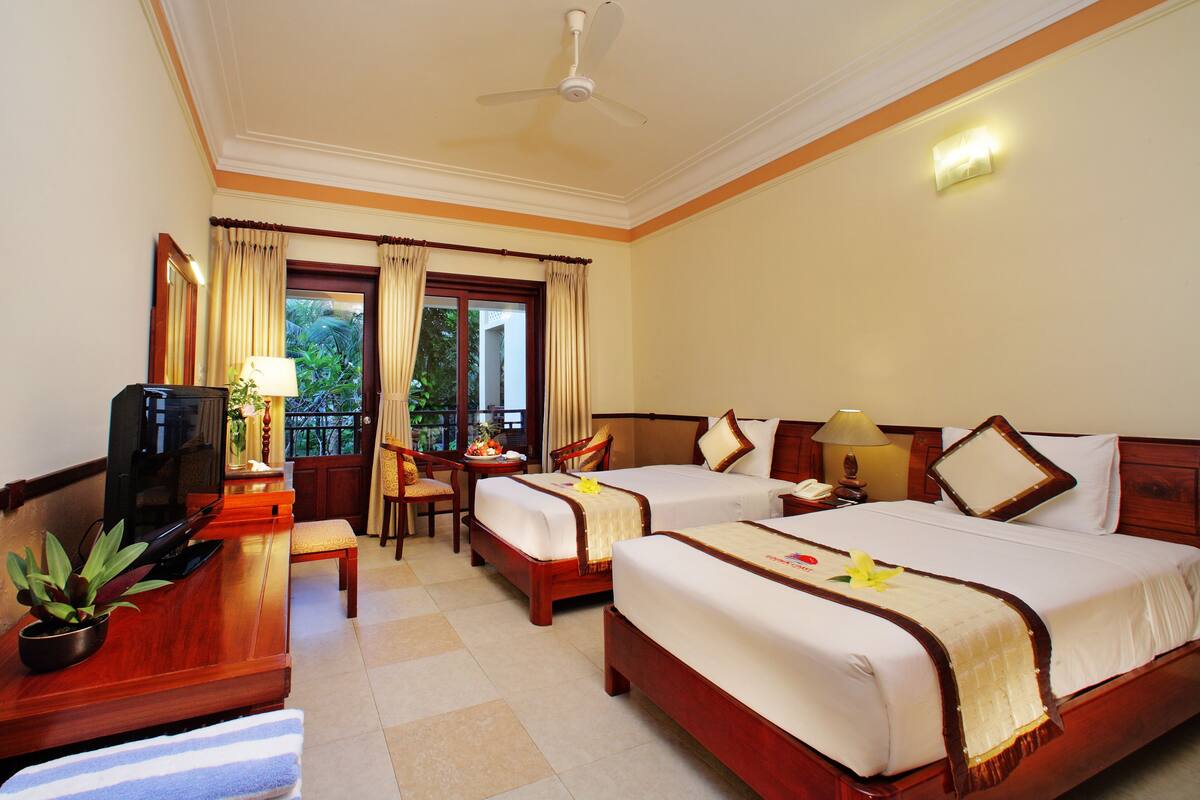 A hotel room with two beds, a desk with a chair, a television, and a potted plant.